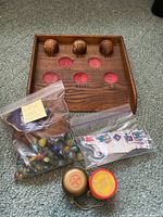 Wooden Skee-Ball style scoring board with three wooden balls, bag of marbles, and bag of postage stamps on carpeted floor.
