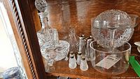 Photo of various glassware items including decanters, salt and pepper shakers with sterling lids, lidded bowl, pedestal bowl, and a glass basket.