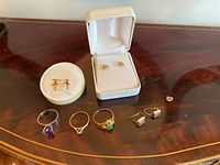 Six gold jewelry pieces displayed on wood table: three rings and three pairs of earrings