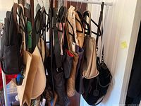 Photo showing a variety of handbags and totes hung on hangers, including beige suede-like bag, woven tote, and black handbags