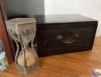 Antique pewter sand timer and Japanese jewelry box side by side on wooden surface showing overall condition and size comparison.
