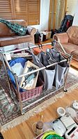 Front view of the metal rolling laundry cart showing gray fabric bags, wicker basket, and some items inside.
