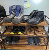 Overview photo of the men's footwear lot showing six pairs including boots, dress shoes, loafers, and sneakers on a wooden shoe rack.