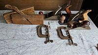 Overview photo of the lot showing two antique wooden planes, two metal C-clamps, and two metal hand planes, including a Stanley plane with wooden handles.