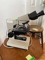 Angled front view showing microscope body, stage, focus controls and power cable on wooden table