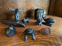 Nine Pueblo Indigenous artisan pottery and carved stone animal figurines displayed on wood shelf, showing variety of styles, animals and shapes.