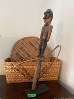 Rectangular and round baskets displayed behind carved figure on stand