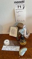 Group of four items: sapphire, oyster shell pendant, gold flakes bottle, candle jar with pink twisted candle