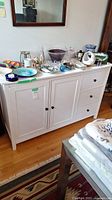 Full view of white painted wood sideboard against a wall with various decorative items on top not included in lot.