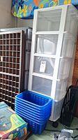 Full view of the white plastic rolling storage drawer system next to the wooden typeset drawer and blue plastic baskets in a garage setting.