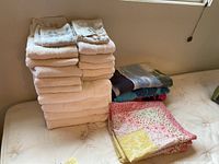Stacked white bath towels with folded pillow shams and patchwork cloth on mattress.