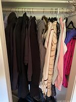 Photo of hanging coats, puffy vests, sweaters in neutral colors, including a light gray puffy vest and a striped sweater.