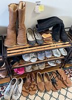 Photo showing assorted women's footwear on metal rack including boots, flats, sneakers, sandals in various colors and styles.