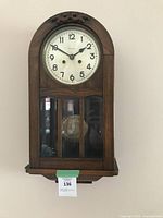 Full image of the wooden box clock mounted on wall showing face and glass pendulum case.