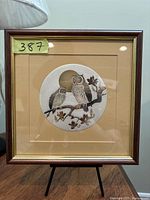 Square framed artwork with two owls on a branch, gold trim, beige matting.
