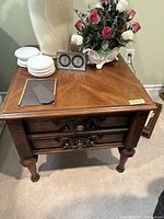 Front view of antique end table with decorative carved drawer fronts, top items removed.