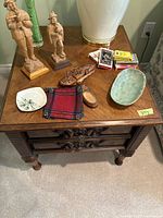 Full view of antique carved oak end table showing top surface and contents on top (not included). Intricate wood carving visible on drawer faces.