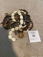 Pile of assorted costume jewelry items including necklaces, bracelets, and pendants on a carpeted floor with auction tag number 41.