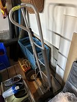 Metal hand truck dolly leaning against a wall near some crates and miscellaneous items.
