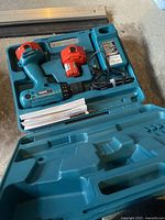 Blue Makita plastic carrying case open showing cordless drill with one battery, spare battery, battery charger and manuals inside.