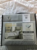 Photo of grey 6-piece queen sheet set packaged in plastic with label showing brand, features, and image of made bed.