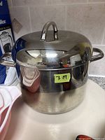 Large stainless steel soup pot with lid, showing reflective polished exterior, two side handles and curved top lid handle