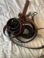 Four men's leather belts in different brown, black, and tan shades, rolled and resting on a striped fabric surface. Visible Danier logo on one belt.