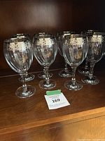 Photo of six vintage 1950s wine glasses with ornate silver rim, arranged on wooden shelf.