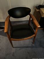 Front view of wooden armchair with black leather seat and backrest on blue carpet against white wall