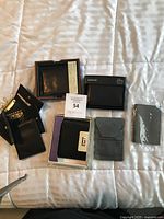 Full lot of seven men's wallets displayed on white and gray striped bed linens.