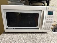 White KitchenAid microwave oven with keypad control and digital display on countertop surface.