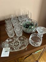 Crystal glassware collection arranged on wooden surface including various cut drinking glasses, bowls, and marbles.