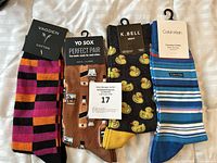Four pairs of men's socks displayed flat on a bed showing various colorful novelty designs and original product tags.
