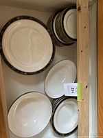 Top view of stacked plates and two serving bowls showcasing the floral black and gold border pattern on white ceramic.