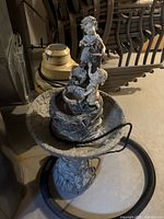 Full view of the outdoor water fountain showing the entire structure with cherub figures and attached hose.