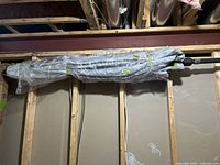 Patio umbrella wrapped in clear plastic, hanging horizontally on interior wall supports under ceiling.