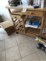 Pine wood portable kitchen island showing drawer, wine rack, open shelving, and tiled top.