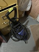 Full view of the blue Simonas power washer sitting on the floor, hose and cord wrapped around it.