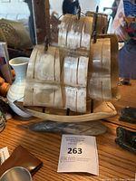 Photo showing the full-sized decorative sailing ship model with translucent sails made of horn or bone material and mounted on a curved wooden base, sitting on a wood surface.