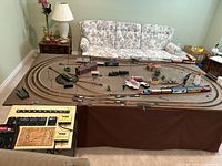 Full layout of the HO scale model train set on a large table with multiple tracks, trains, buildings including a station and engine house, and accessories.