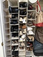 Photo showing multiple pairs of women's shoes neatly placed in hanging fabric organizers with compartments. Various styles and colors visible including black, brown, beige, white.