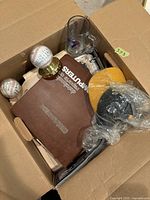 Overhead view of open cardboard box showing baseballs, sports card binder, glass mug, wrapped hockey pucks and other items