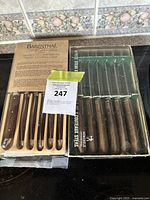 Two sets of steak knives: one Barenthal set in its box on the left with six knives having wooden handles, and one Henckels set on the right partially open showing six steak knives with wooden handles.