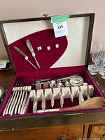 Wooden box open showing red felt interior with cheese knives on lid and main flatware in base