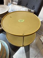 Side view of round two-tier Lazy Susan showing mustard yellow plastic trays and metal rod center support.