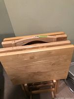 Top down view of four wooden TV folding tables stacked together showing light wood grain finish and folded legs.