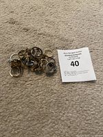 Pile of assorted costume jewelry rings on beige carpet next to auction lot marker