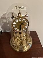 Vintage Kien 400-day torsion clock under clear glass dome on brass base, clock face with Roman numerals and ornate black hands.