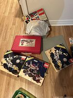 Plastic tub of loose LEGO bricks, red carrying case, multiple instruction manuals on floor