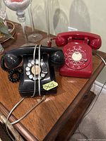 Photo of two vintage rotary phones, one black and one red with Bell logo, placed on a wooden surface.